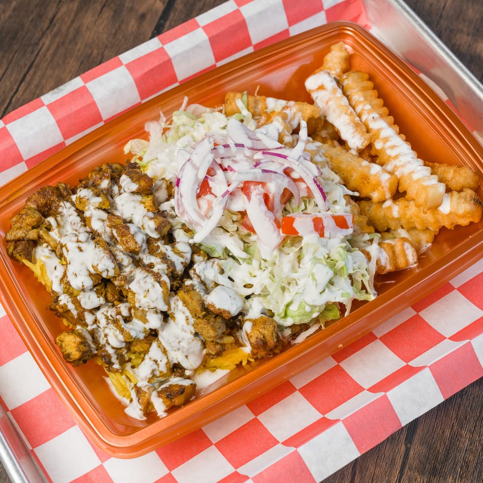 Chicken and rice platter with salad, crinkle-cut fries, and white sauce on checkered paper.