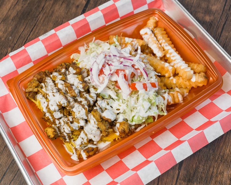 Chicken and rice platter with salad, crinkle-cut fries, and white sauce on checkered paper.