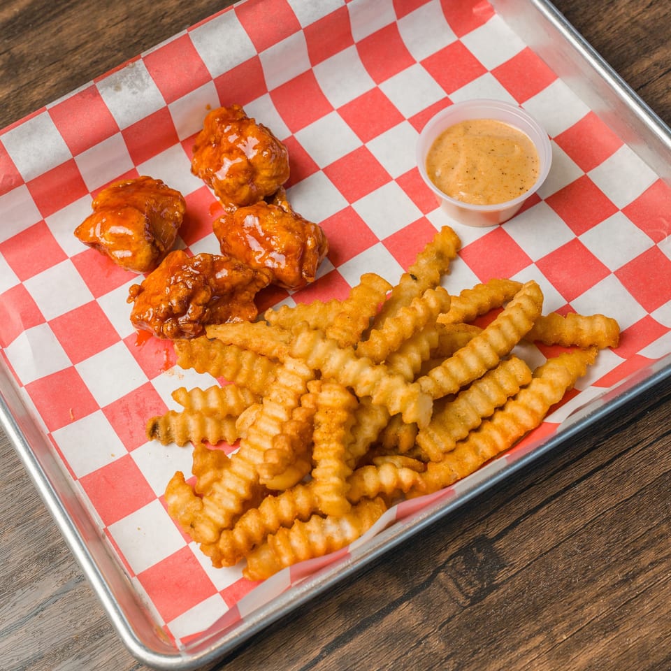 Boneless chicken wings, crinkle-cut fries, and dipping sauce on a metal tray with checkered paper.